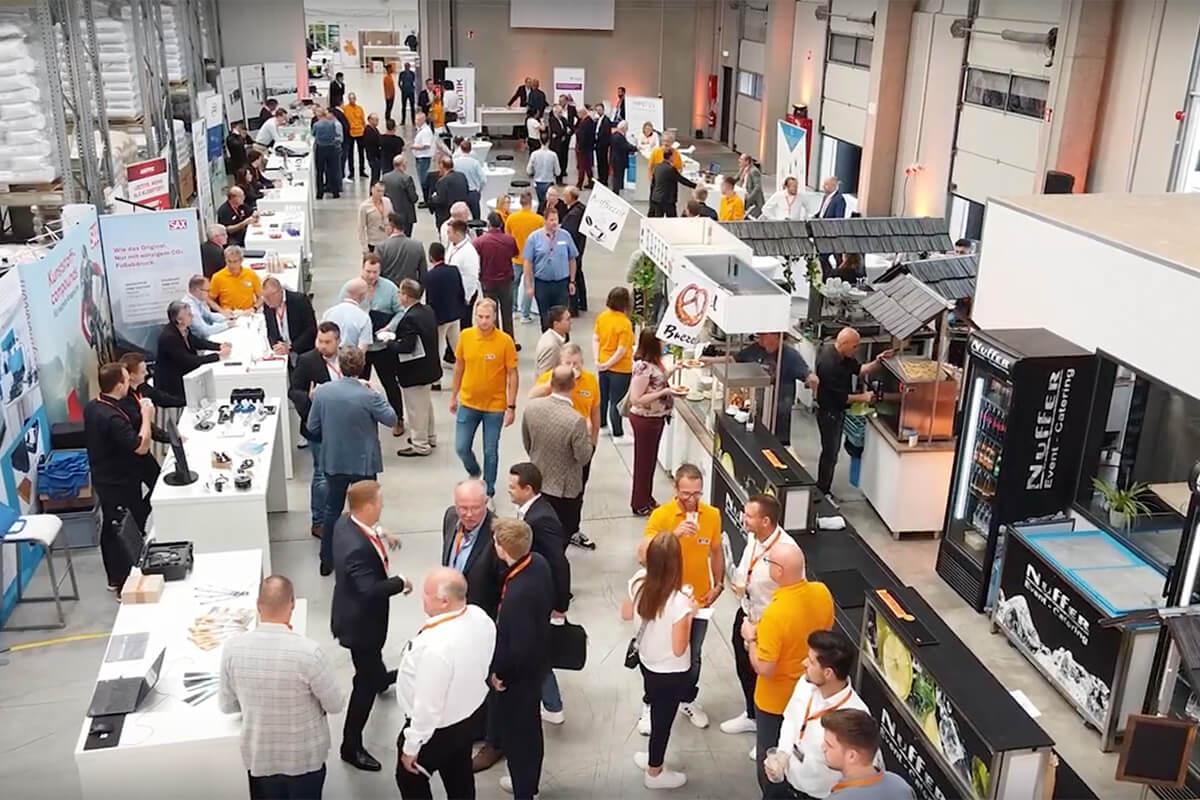 Geschäftsmesse mit Besuchern an Ständen in einer Halle, Networking und Catering im Vordergrund.
