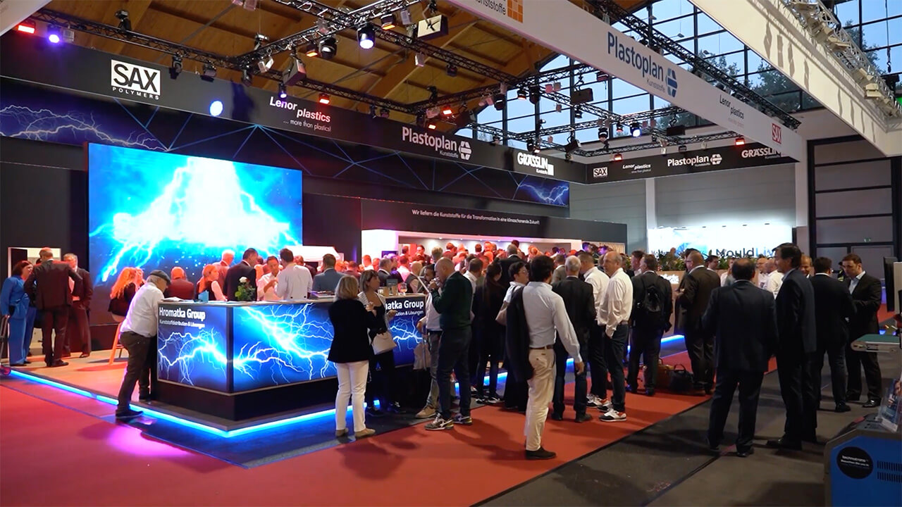 Messebesucher versammeln sich am modernen Stand von Plastoplan mit leuchtenden Displays und dynamischer Atmosphäre.