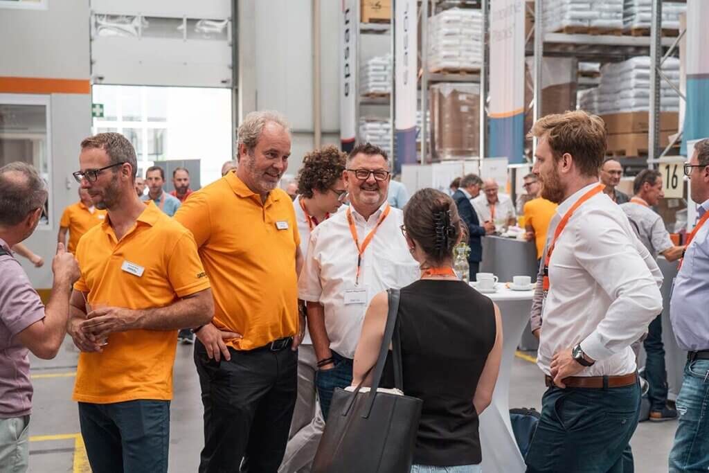 Mitarbeiter in orangefarbenen Hemden unterhalten sich bei einer Networking-Veranstaltung in einem modernen Lager.