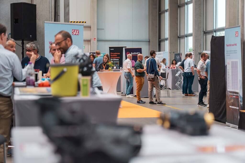 Messehalle mit geschäftigen Ständen und Menschen im Gespräch, Networking auf einer Konferenz oder Ausstellung.