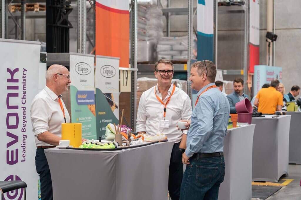 Geschäftsleute im Gespräch auf einer Messe, Evonik-Stand im Hintergrund. Networking und Business-Event.