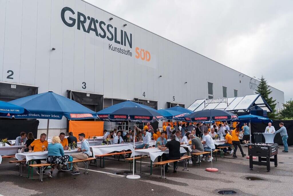 Mitarbeiterfest bei Grässlin Kunststoffe mit Gästen unter blauen Sonnenschirmen und lebhafter Atmosphäre.